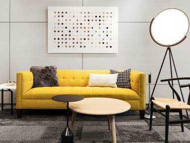 A yellow sofa in a lounge area with a Wishbone chair from Coalesse and Superloon lamp from FLOS next to it