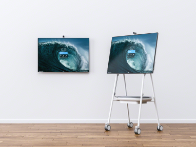 A Steelcase Roam cart holding an electronic screen is shown next to a screen attached to a white wall