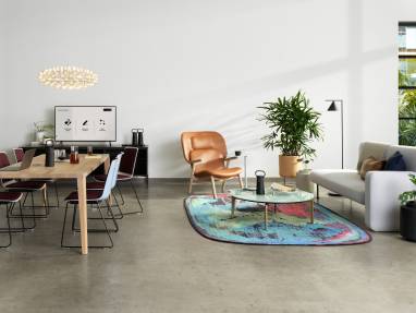 Ancillary setting with a variety of Partner products, that includes a gray Bolia Pebble Sofa, a white oak Bolia Graceful Dining Table, plum and white Nooi Seating, and a colorful Moooi rug.