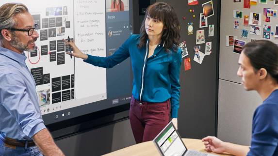 Three people work together around an electronic whiteboard