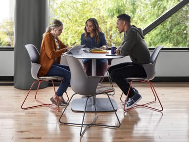 Three people have a conversation at an Enea Lottus Table while sitting on Node X base chairs