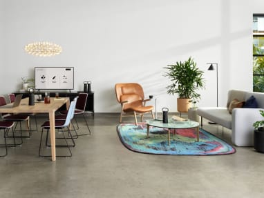 Ancillary setting with a variety of Partner products, that includes a gray Bolia Pebble Sofa, a white oak Bolia Graceful Dining Table, plum and white Nooi Seating, and a colorful Moooi rug.