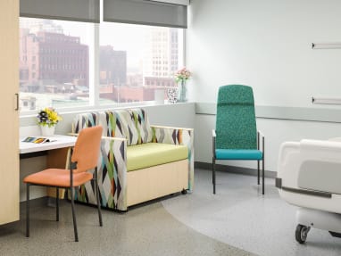 inside an hospital room with an orange sorrel chair in front of a table, a 1-person sofa next to it