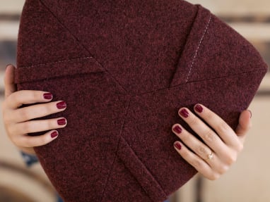 A woman's hands with burgundy-painted nails holding a burgundy Turnstone Campfire Pouf.
