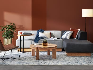 A collection of West Elm Work products in a lounge setting, including a Conover Plinth armless sofa, Conover Plinth ottoman, Boerum coffee table, Slope lounge chair, and Linear C-Table