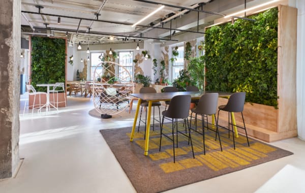 Stools from the Viccarbe collection are arranged around a Coalesse Potero415 table in front of a living plant wall from the Sagegreenlife collection
