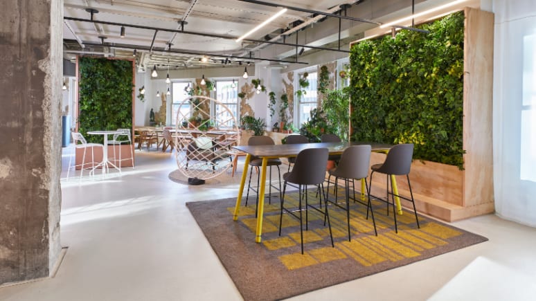 Stools from the Viccarbe collection are arranged around a Coalesse Potero415 table in front of a living plant wall from the Sagegreenlife collection