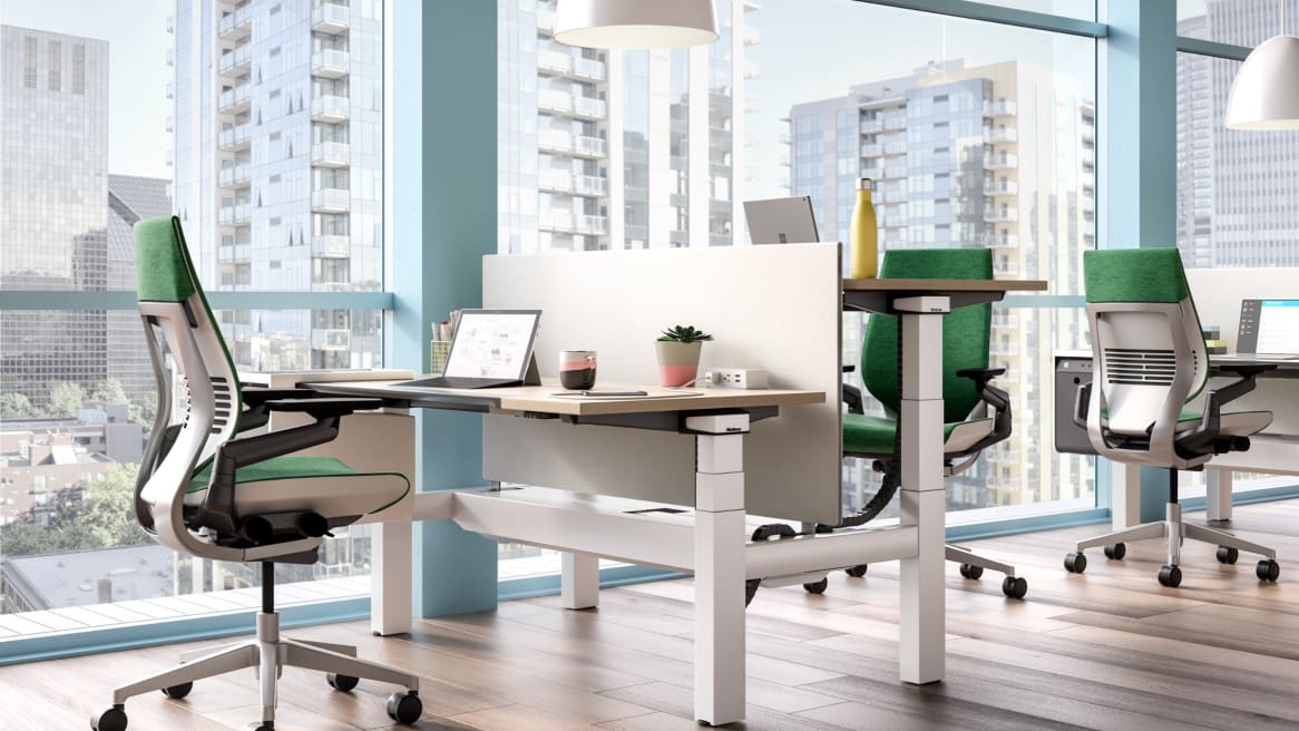 Ology height adjustable benching next to a window and shown with Gesture desk chairs, Universal Center Screen, and SOTO Personal Console