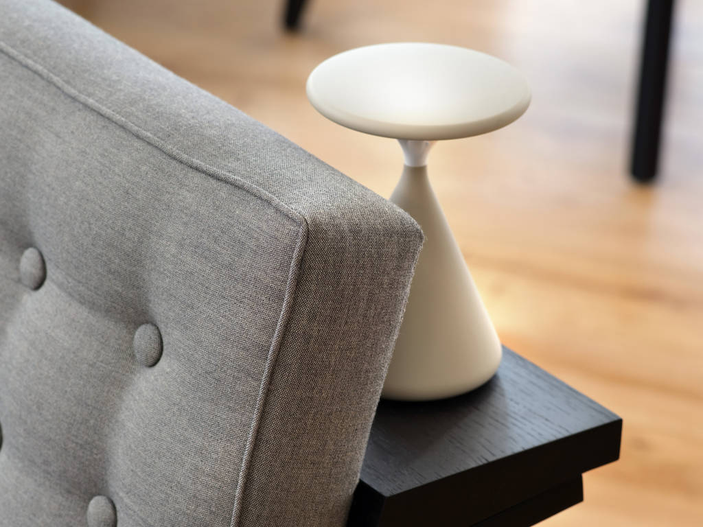 Corner of a grey sofa and a white lamp behind it.